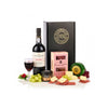 A curated gift set featuring a bottle of Vista Alegre Fine Bodegaria Port wine, a glass of red wine, a black box with gold lettering, a pink box labeled Bineaghs, a green and gold cheese wheel, a small round cheese container, and assorted cheeses and cured meats arranged on a white background with grapes and red berries as props.