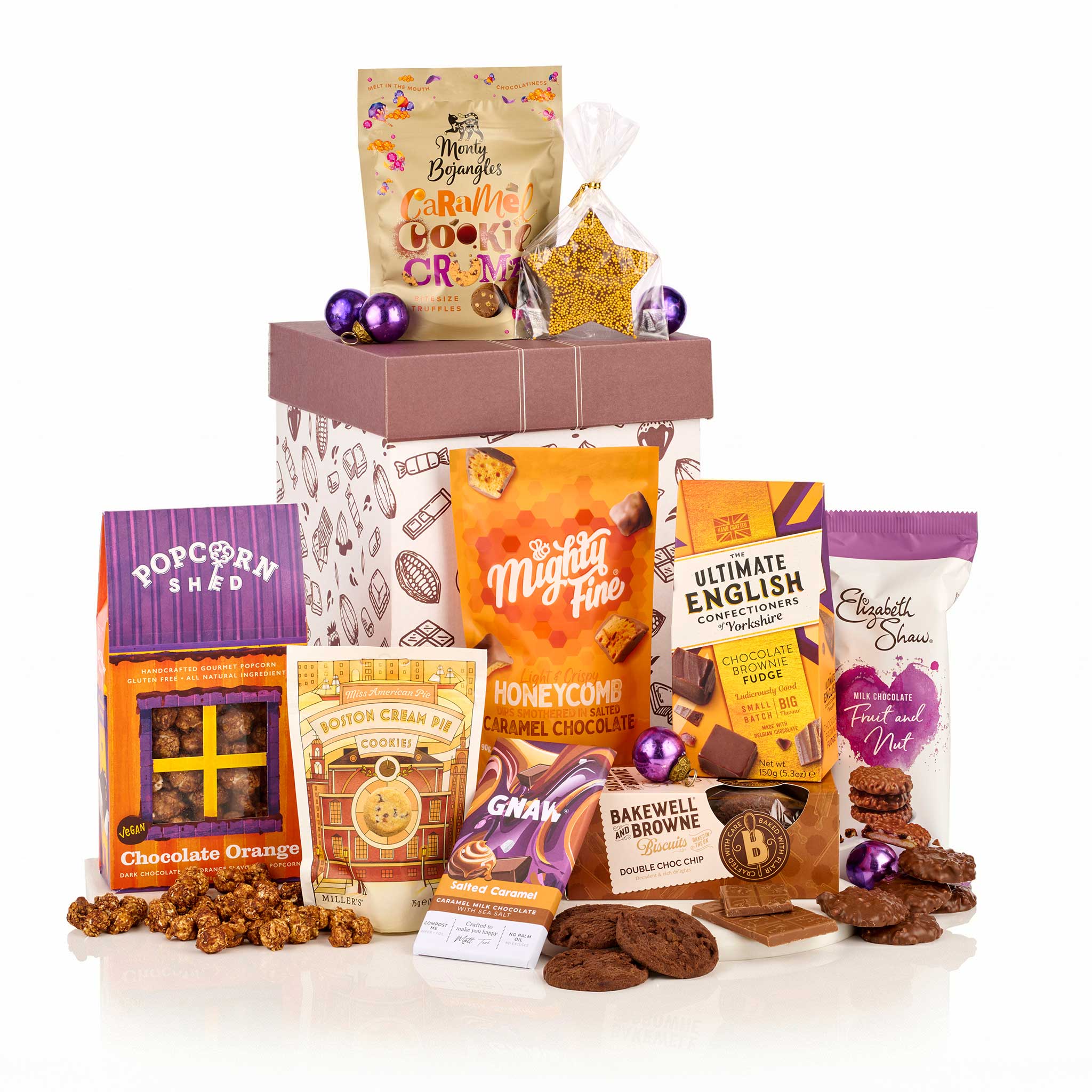 A curated gift basket of assorted snacks and chocolates from brands like Mighty Fine, Elizabeth's, and Popcorn Snaps, arranged around a patterned gift box on a white background.