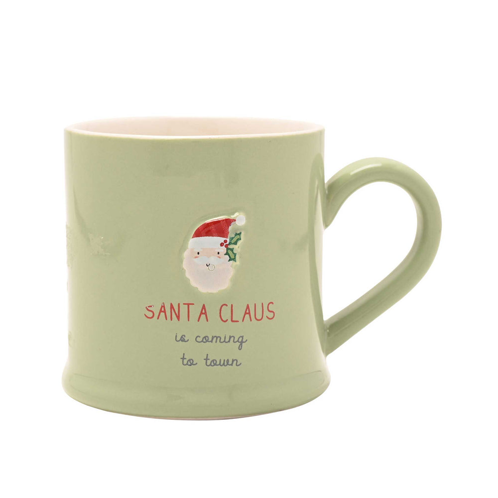 A light sage green ceramic mug with a handle, featuring a graphic of Santa Claus and the text 'SANTA CLAUS is coming to town' on a plain white background.