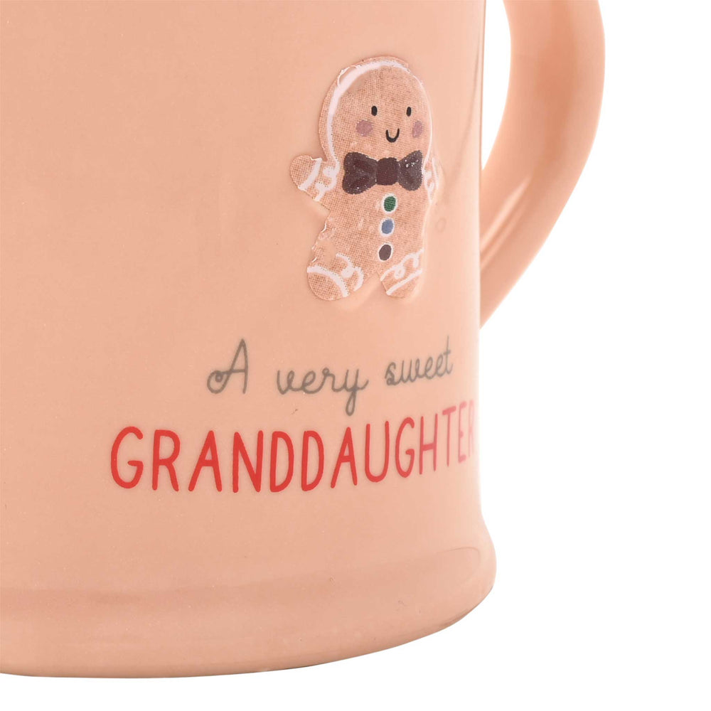 Close-up of a peach-colored ceramic mug with a gingerbread man decoration and the text 'A very sweet GRANDDAUGHTER' on a white background.