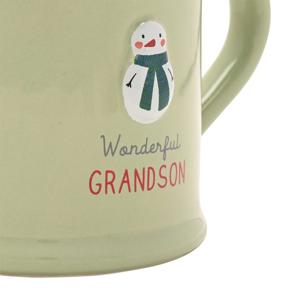 Close-up of a light sage green ceramic mug with a handle, featuring a small snowman illustration and the words 'Wonderful GRANDSON' on the front.