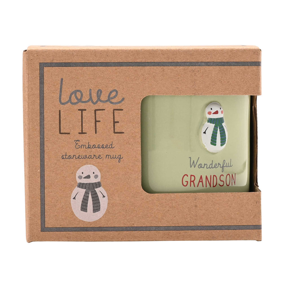 A boxed engraved stoneware mug with a kraft paper presentation box. The mug is pale green and features a snowman design with the words 'Wanderful GRANDSON.