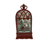 A Christmas-themed clock or lantern with a dark reddish-brown wooden frame and a glass window showing a festive winter scene with Santa Claus, evergreen trees, and snow, set against a plain white background.