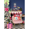 A festive holiday interior scene with a decorated silver Christmas tree, pink armchair with a colorful 'FALA LALA' throw pillow, pink gift box, fireplace mantel with holiday decor, and a dark blue wall.