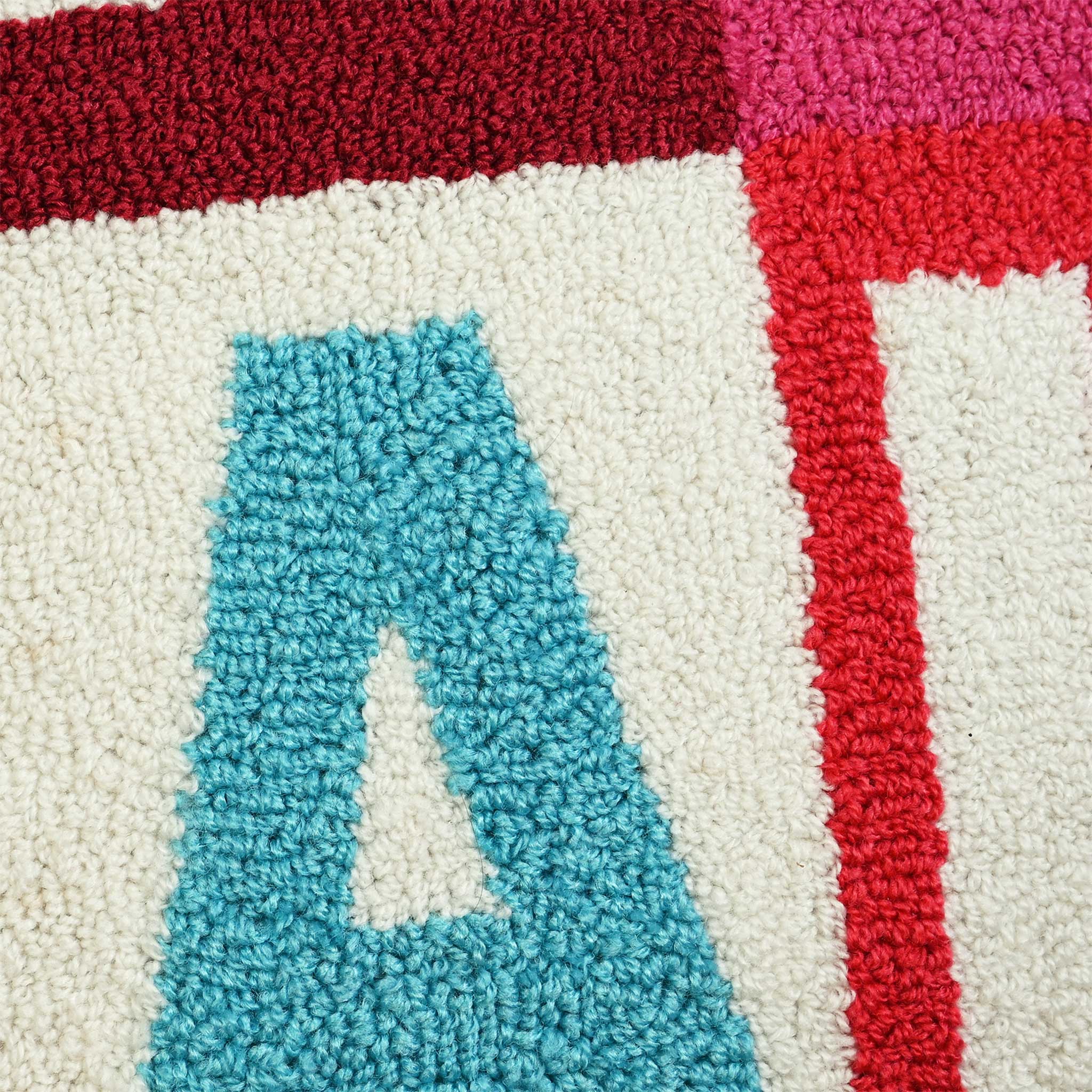 Close-up of a pillow showing a large turquoise letter A on an off-white background, bordered by red and magenta sections.