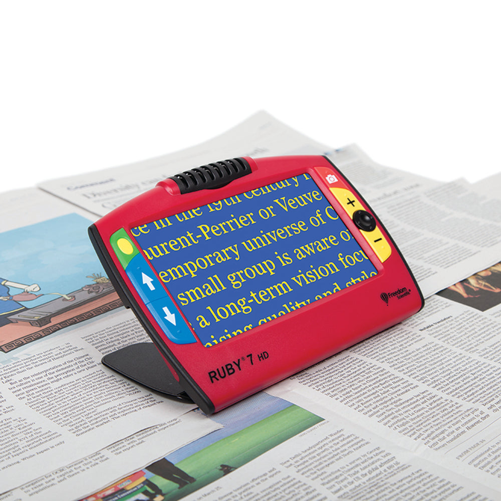 Magnifier sitting on newspaper and displaying magnified text in a yellow on blue format on its screen