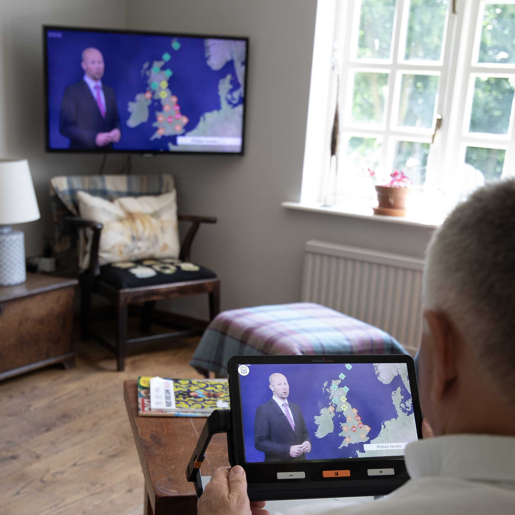 A man uses the Explore 12 to magnify his television and watch the weather forecast