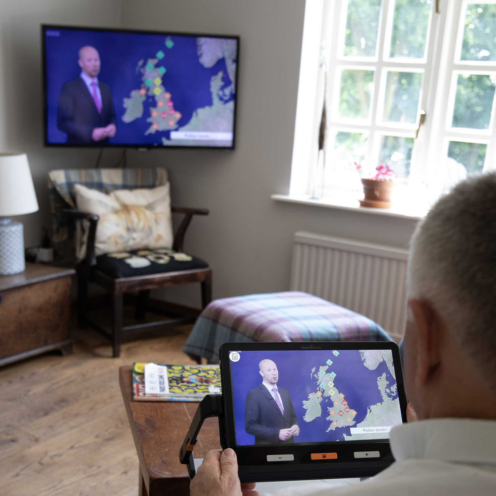 A man uses the Explore 12 to magnify his television and watch the weather forecast