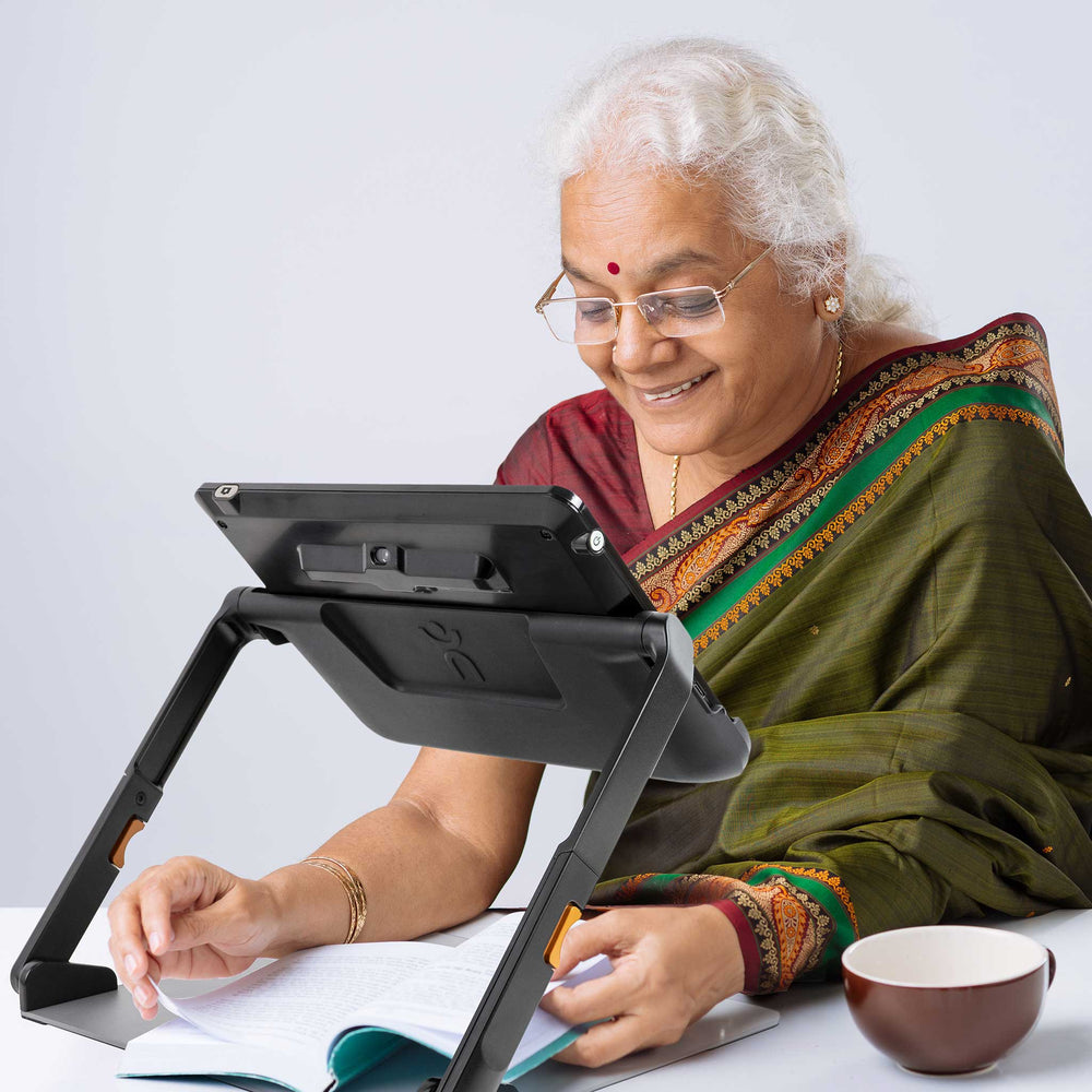 An older woman in red and green sari uses the Explore 12 to read a book at a table