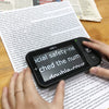 Luna S portable video magnifier with enlarged white on black text above standard text on an A4 sheet