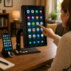 A woman at a wooden desk uses a large tablet mounted on a black stand, with a smartphone on a small stand beside it in a home office setting.