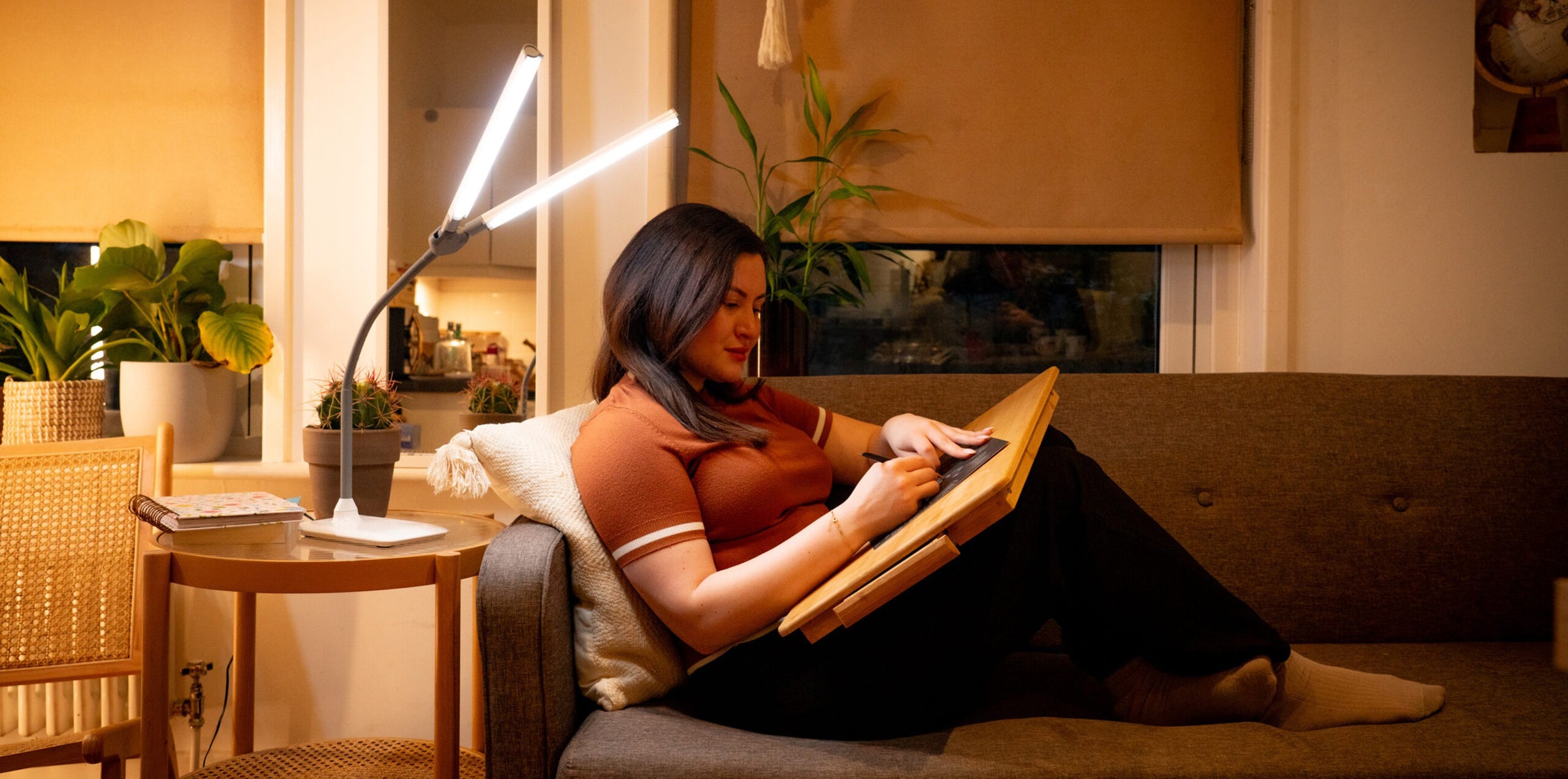 A woman sits with her feet up on a sofa, drawing using the light from a DuoLamp