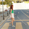 A light-skinned woman with long red hair using a pedestrian crossing with a wewalk 2 cane