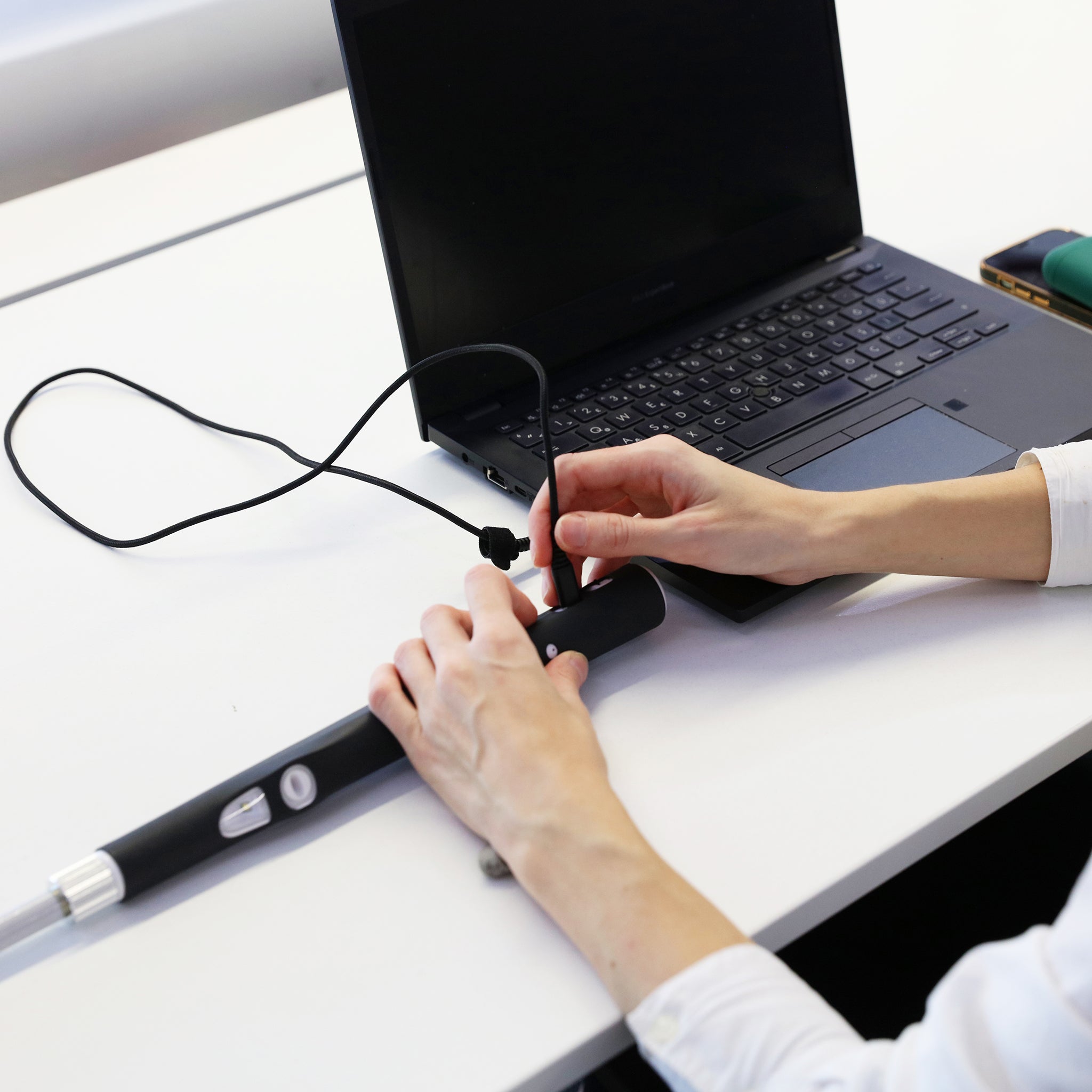 A person attaching a charging cable that runs from a laptop to the smart cane