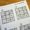 Sudoku puzzle book sowing puzzle solutions on a wooden surface