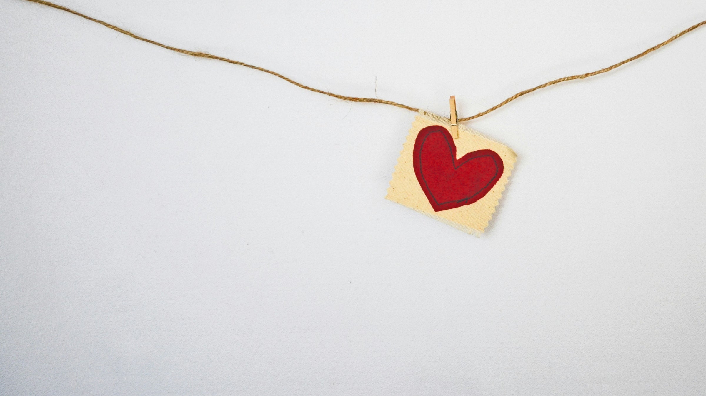 Red heart drawn on a small piece of paper clipped to a string against a white background.