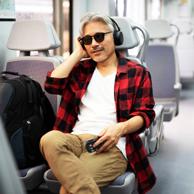 Lifestyle image shows man on a train holding product with headphones in