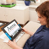 A woman sitting at table reading a newspaper with the traveller HD portable video magnifier