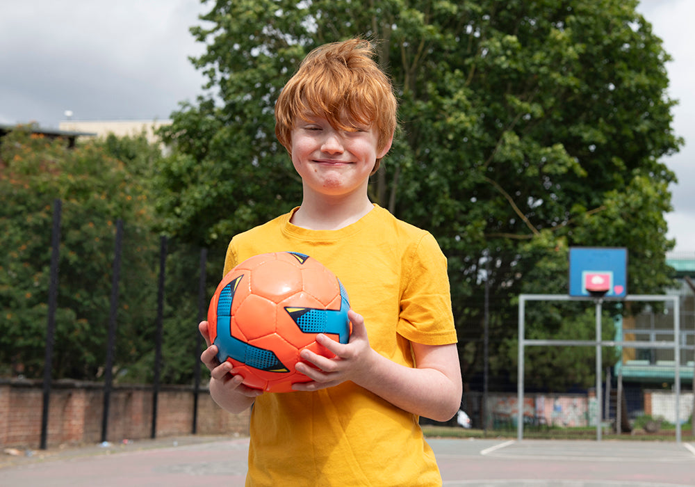 A young person with red hair and a yellow T-shirt is smiling and holding an audible football.