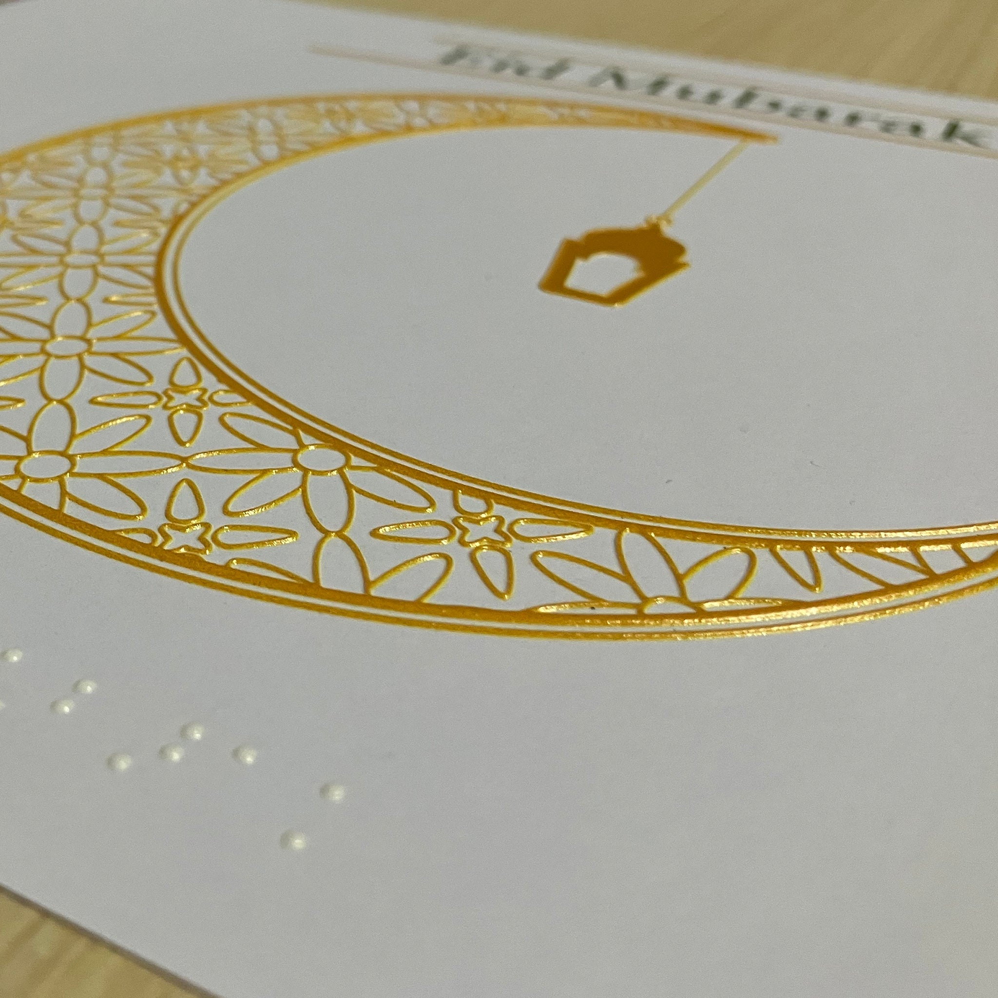 Decorative card with gold crescent moon and Arabic text on a white background