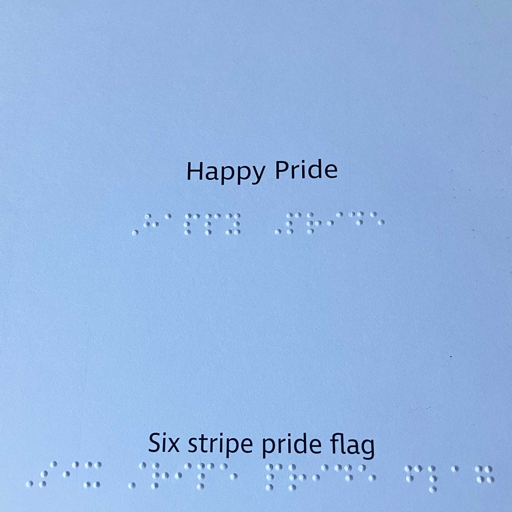 Text inside the card with 'Happy Pride' and 'Six stripe pride flag' on a blue background with braille text.