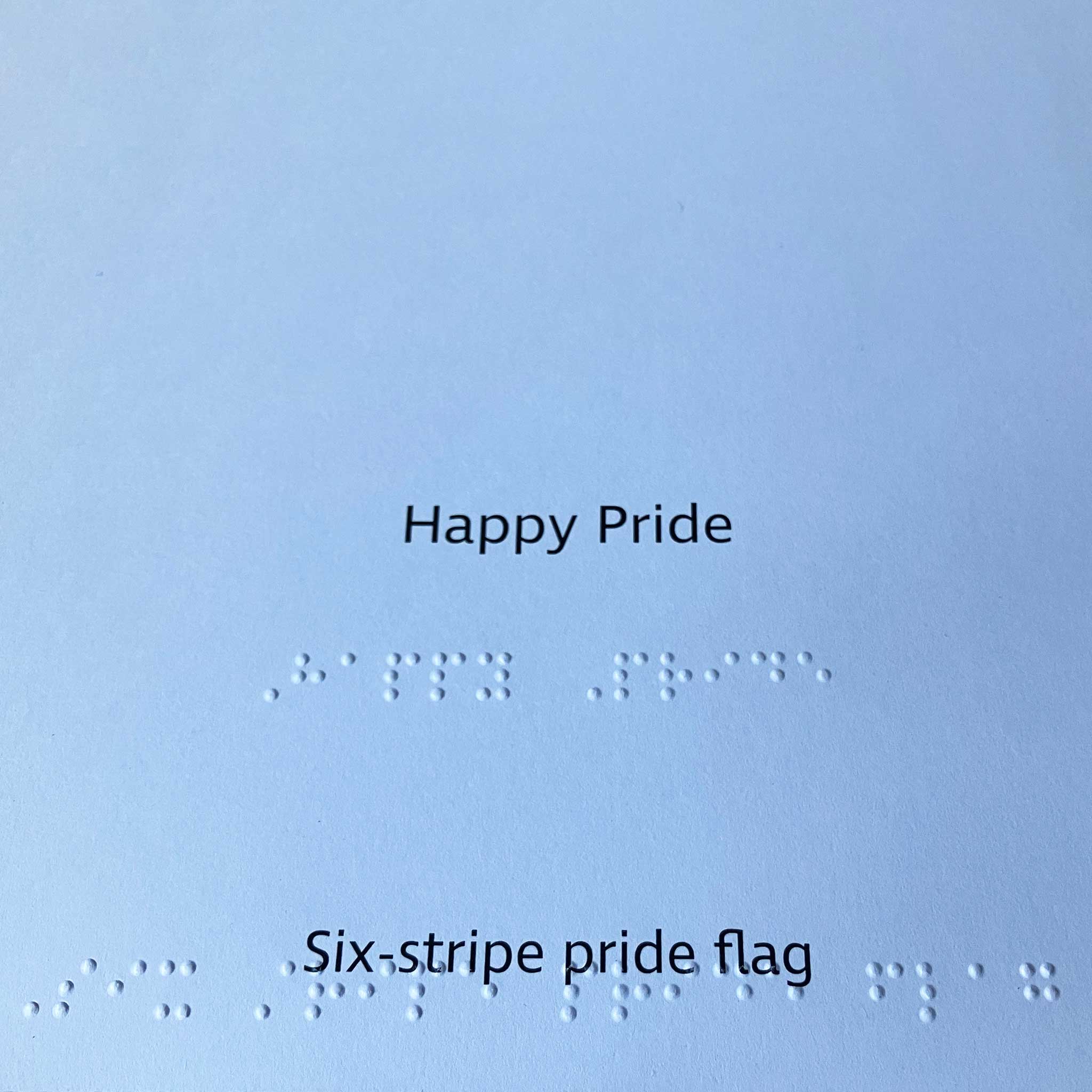 Text 'Happy Pride' and 'Six-stripe pride flag' on a white background with braille text.