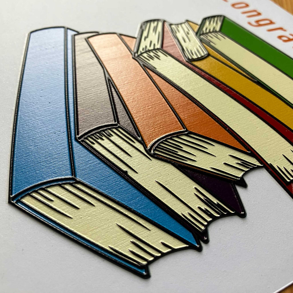 A close-up of a colorful book illustration showing several fanned-out books in blue, beige, peach, orange, yellow, and green on a white background.