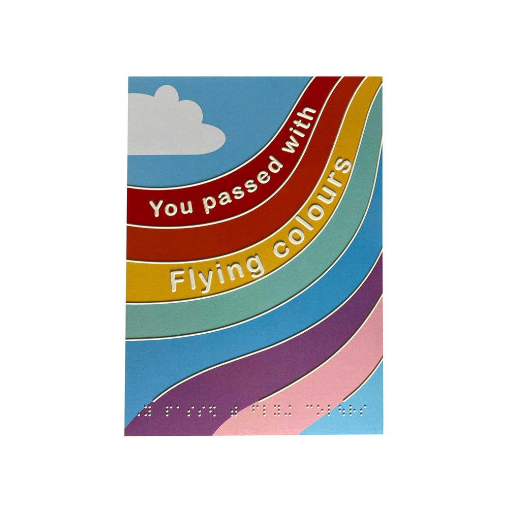 A colorful printed card or poster with curved rainbow-like stripes in blue, red, yellow, green, purple, and pink, plus a white cloud and the text 'You passed with Flying colours.' in print and braille.