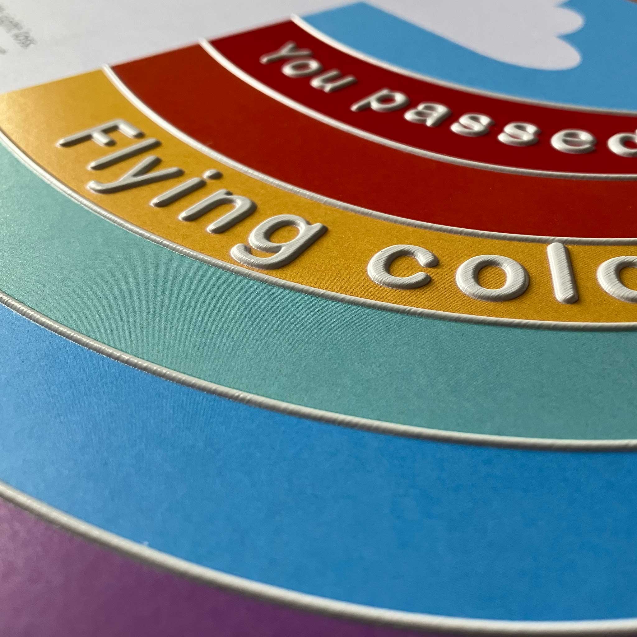 Close-up of a colorful circular graphic with embossed text reading 'You passed Flying color', teal, gold, red, and purple.