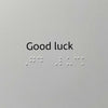 Card with the words 'Good luck' in black serif text above braille dots on a light gray background.