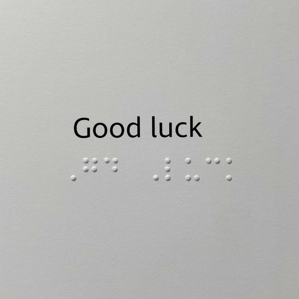 Card with the words 'Good luck' in black serif text above braille dots on a light gray background.