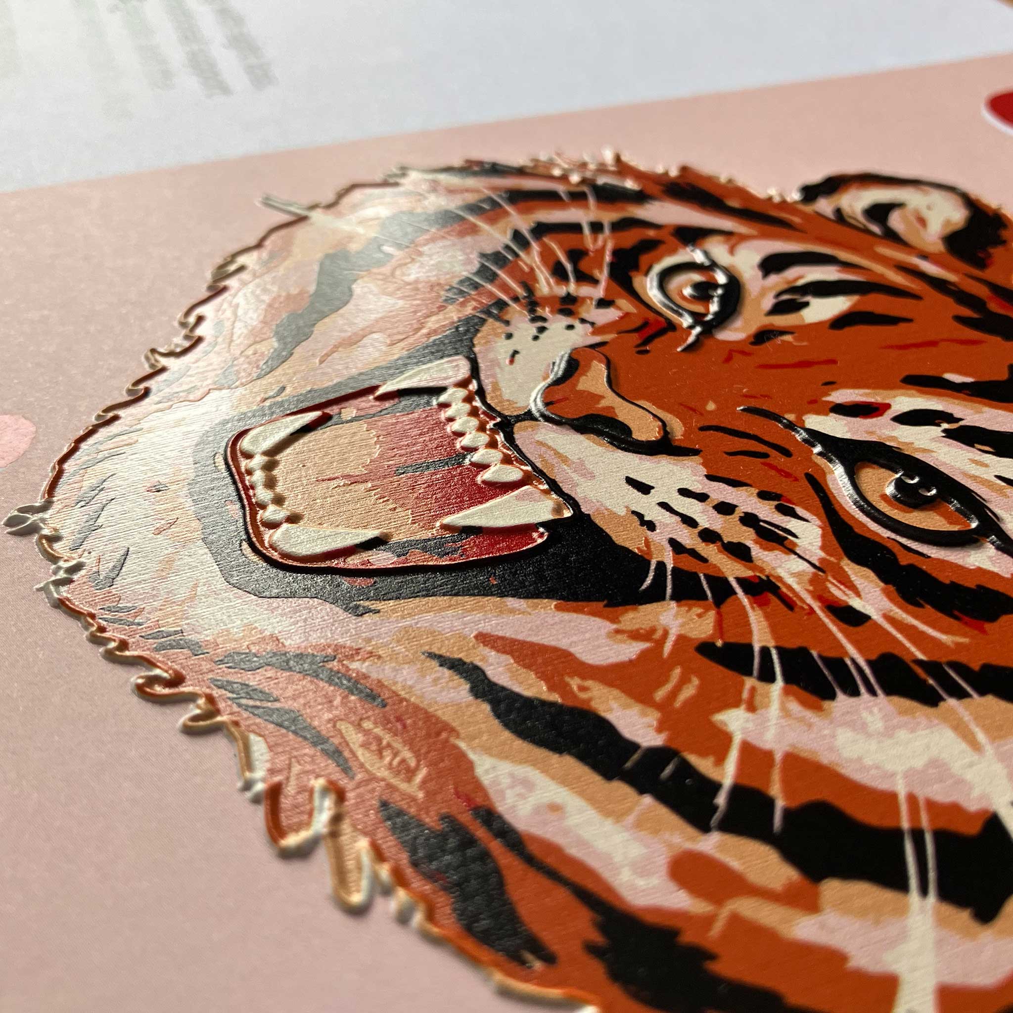 A close-up of  a stylized tiger face in orange, black, cream, and red tones, placed on a pink surface.