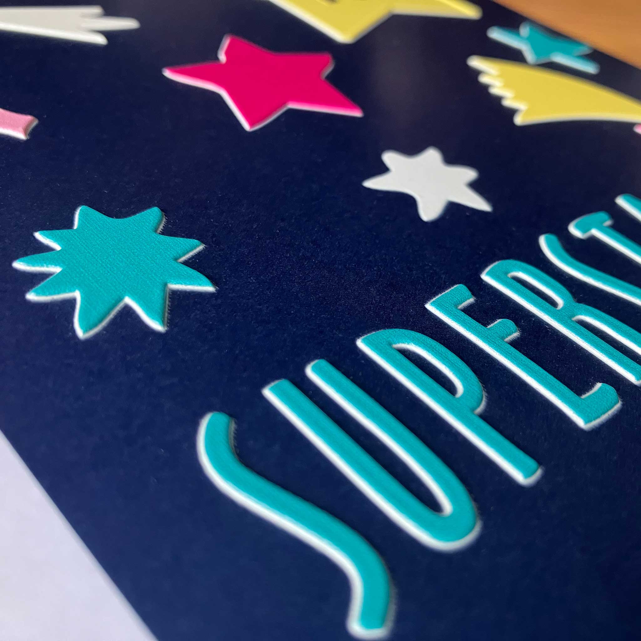 Close-up of the card which has a dark navy blue surface with colorful star and burst shapes in pink, yellow, teal, and white.