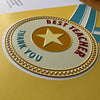 A close-up of the card or with a gold embossed star, red 'BEST TEACHER' text, and blue 'THANK YOU' text on a yellow background.