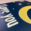 Card with 'I love you' text and a yellow crescent moon on a blue background