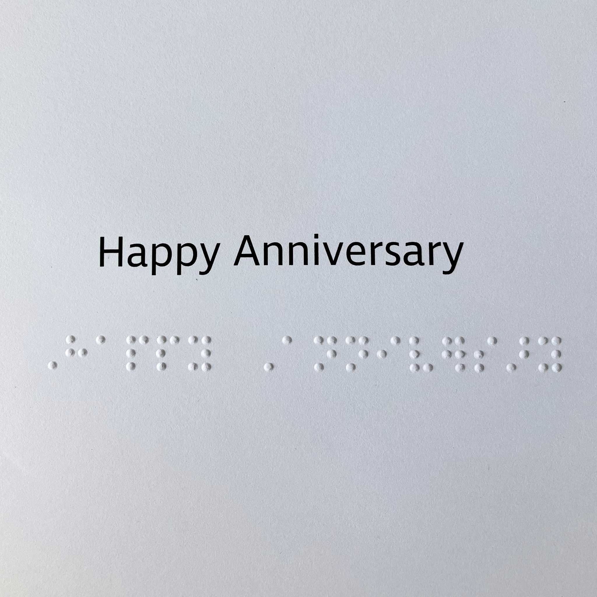 Card greeting 'Happy Anniversary' in black text above contracted braille.