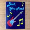 Deep purple 'Dad, you rock' card with red electric guitar design on a wooden desk