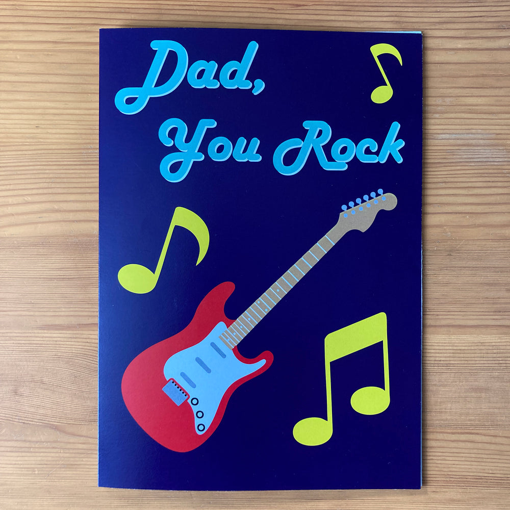 Deep purple 'Dad, you rock' card with red electric guitar design on a wooden desk