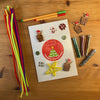 Recordable card on a desk with tactile decorating elements - colourful pipe cleaners, glitter, wooden Highland cows, glittery buttons and festive cardboard buttons