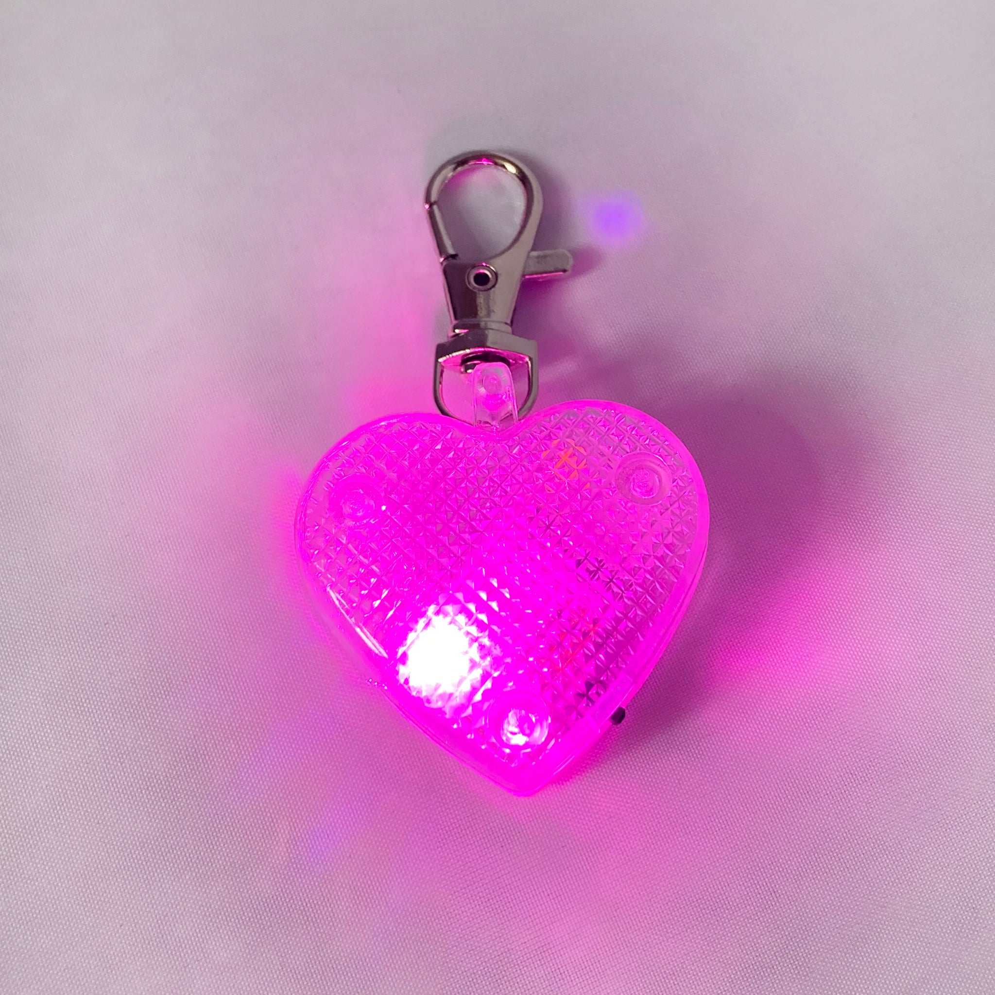 Heart-shaped light-up dog tag on white background with pink light flashing