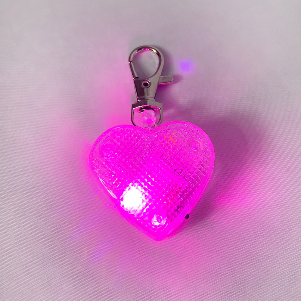 Heart-shaped light-up dog tag on white background with pink light flashing
