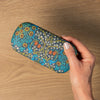 Hand holding a floral-patterned glasses case on a wooden surface.