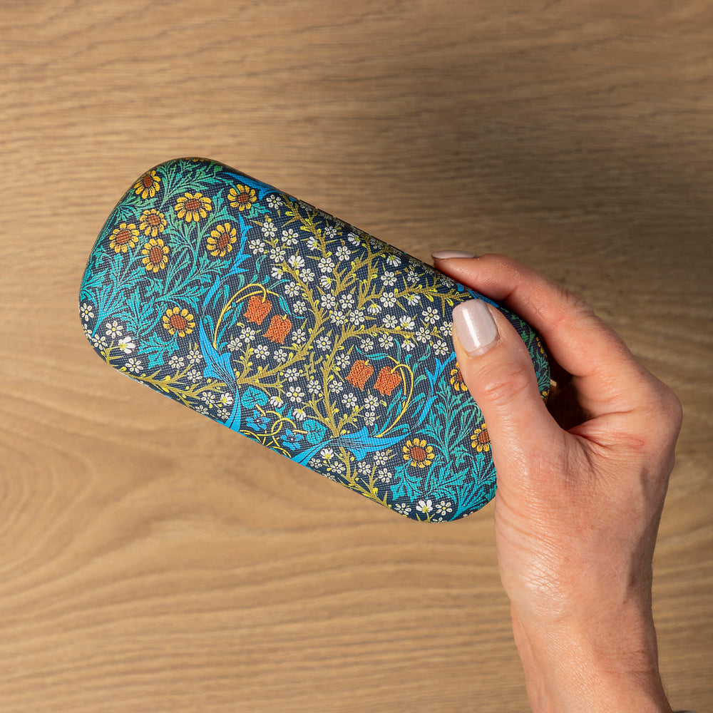 Hand holding a floral-patterned glasses case on a wooden surface.