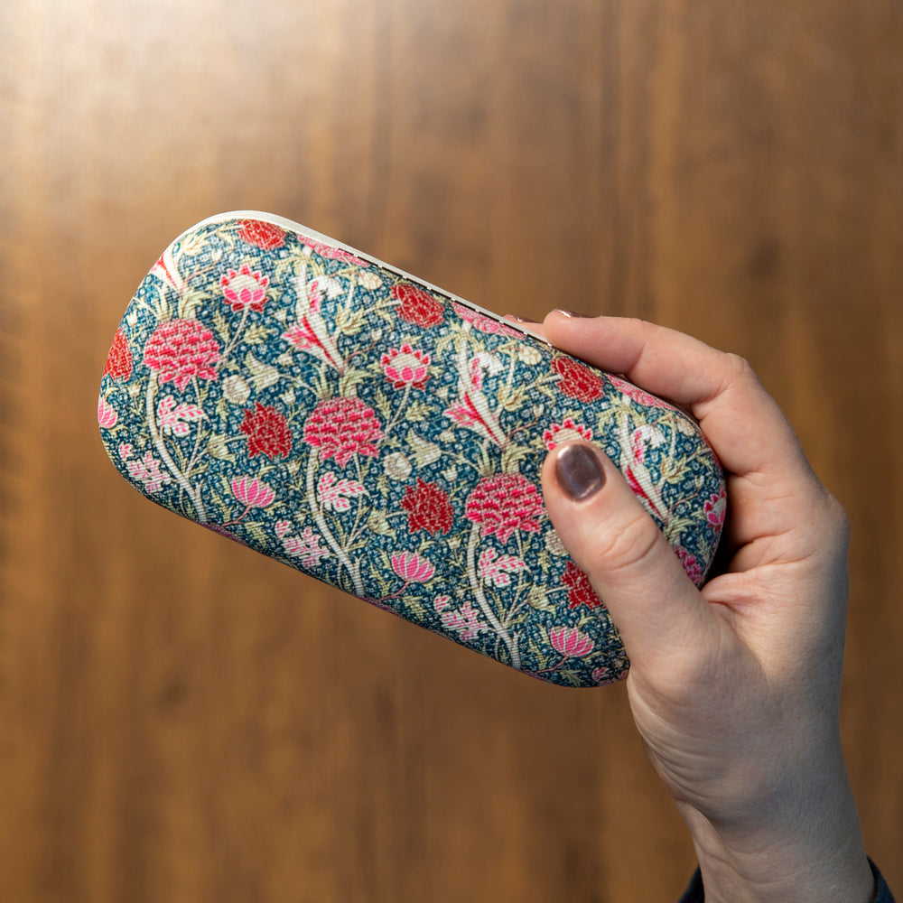 Hand holding a floral-patterned glasses case against a wooden background.