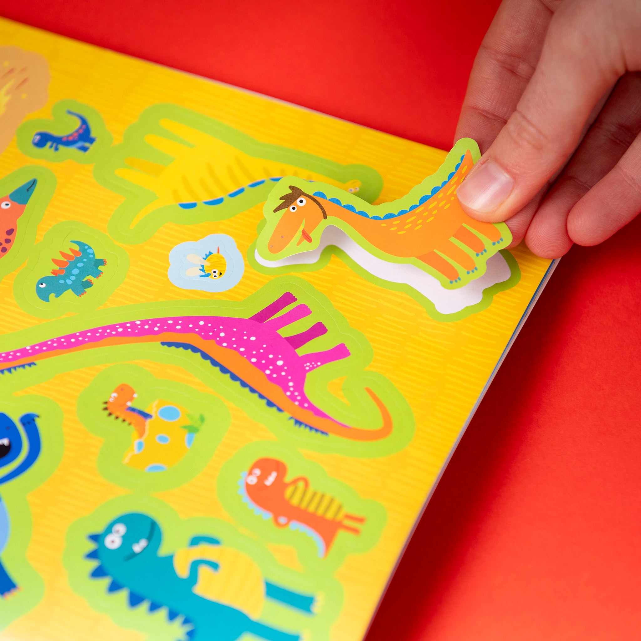 Colorful dinosaur-themed book with a hand interacting with the pages on a red background