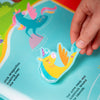 Hand holding a colorful sticker of a unicorn over a children's book with illustrations.