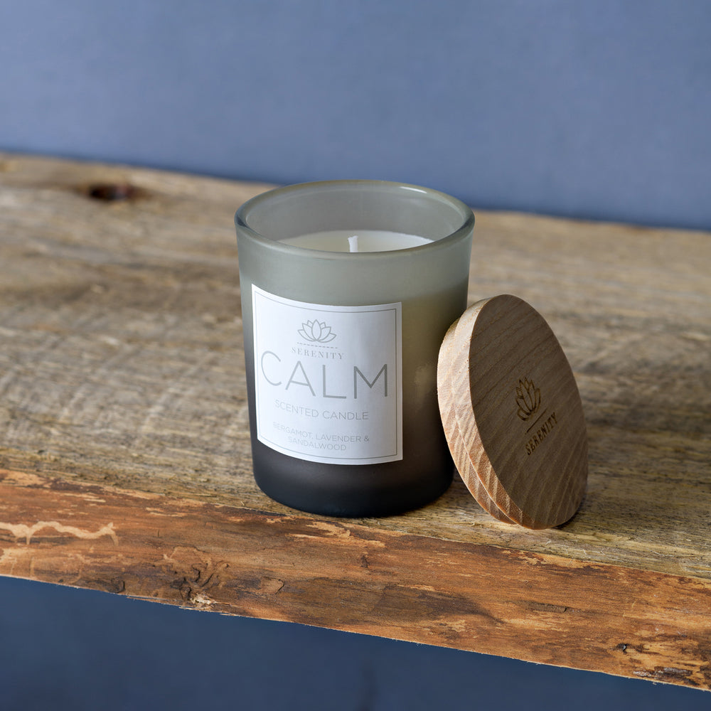 Candle labeled 'CALM' with wooden lid on a wooden surface against a blue background
