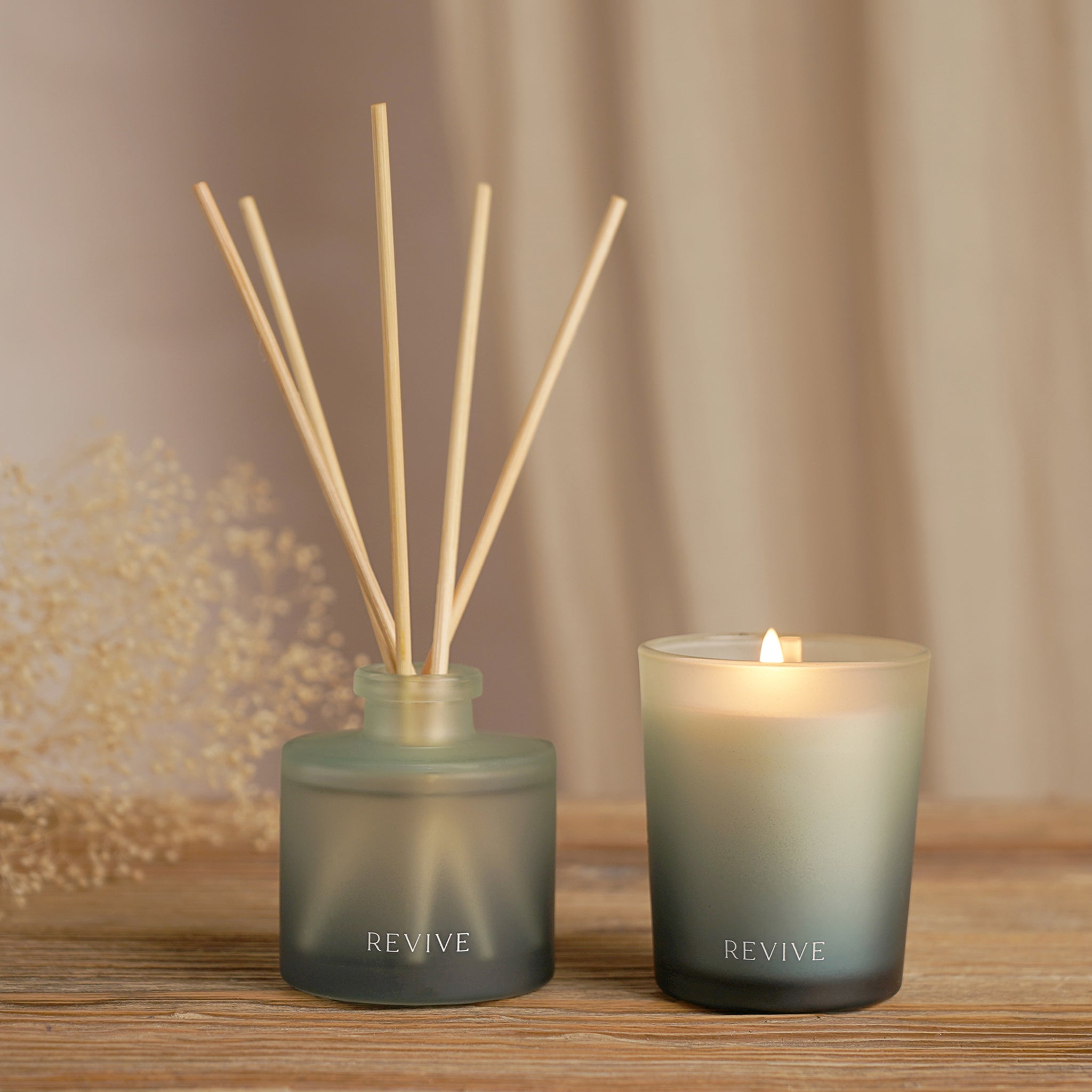 Two 'REVIVE' diffusers, one with sticks and the other a candle, on a wooden surface.