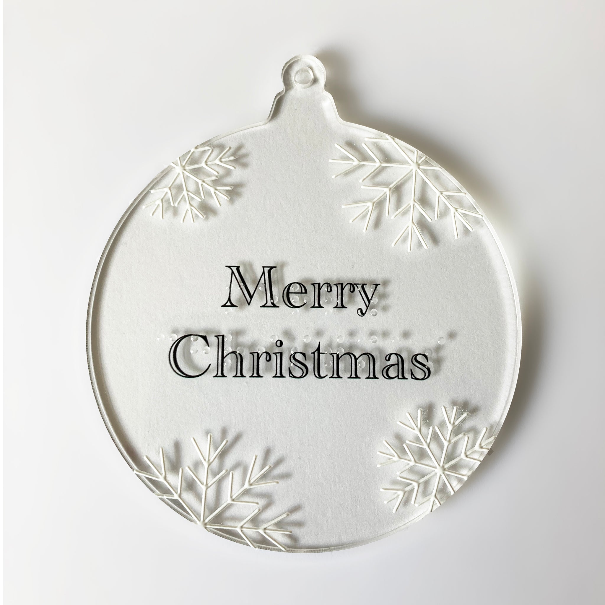 Round Christmas ornament with 'Merry Christmas' text and braille with snowflake designs on a white background.