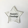 Star-shaped decorative ornament with 'Season's Greetings' in text and braille  on a white background